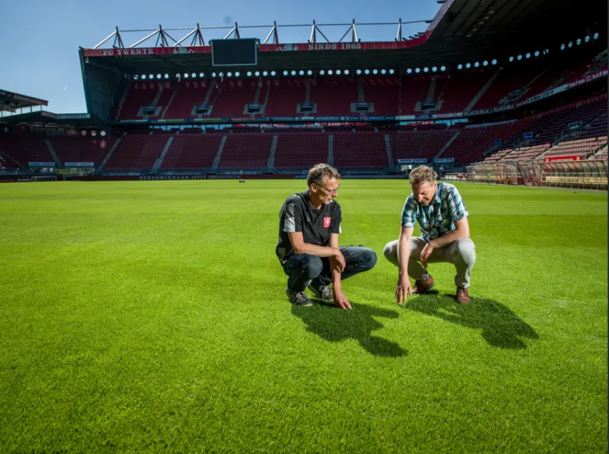 Twee mannen bekijken de grasmat in het stadion van FC Twente