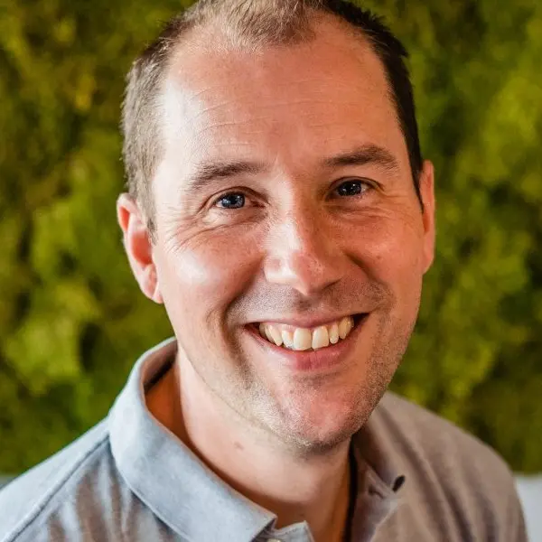 Portret van Joeri Faas in grijze polo, lachend voor een mosmuur