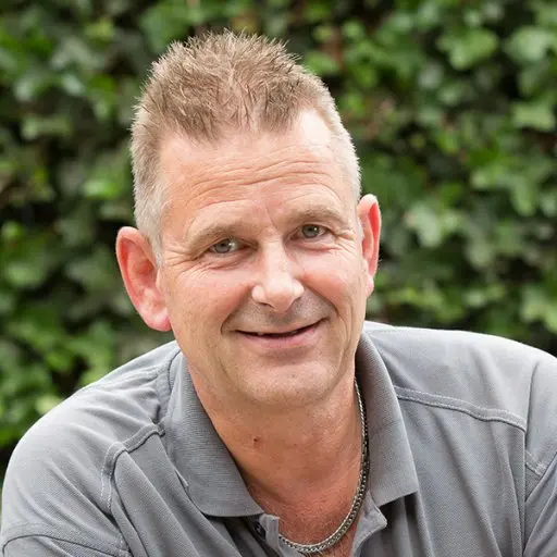 Portret van Richard Schoonhoven met kettinkje voor een groene klimopmuur
