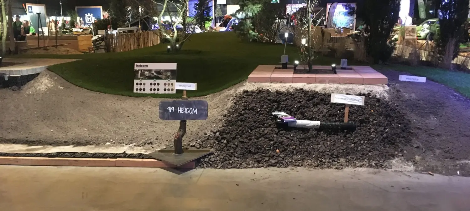 Beursvak met hopen zand en zwart granulaat en een bordje Heicom
