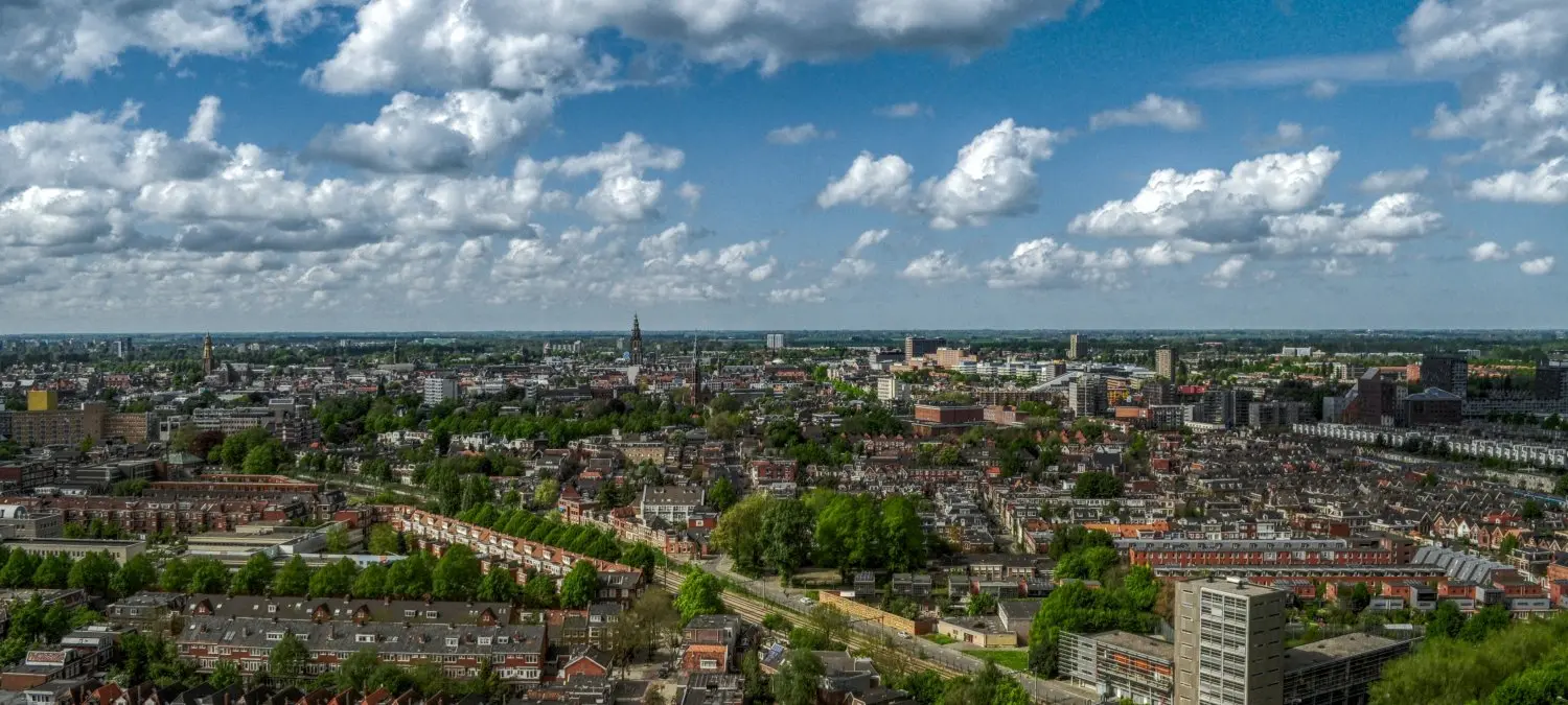 Panorama over een stad met woonwijken, groen en wolkenlucht