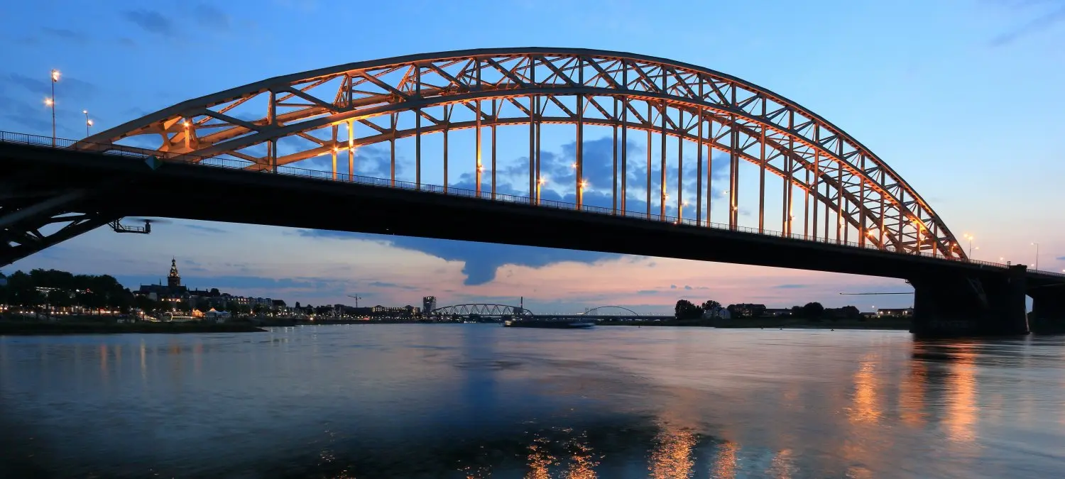 Verlichte stalen boogbrug over de Waal bij Nijmegen in de schemering
