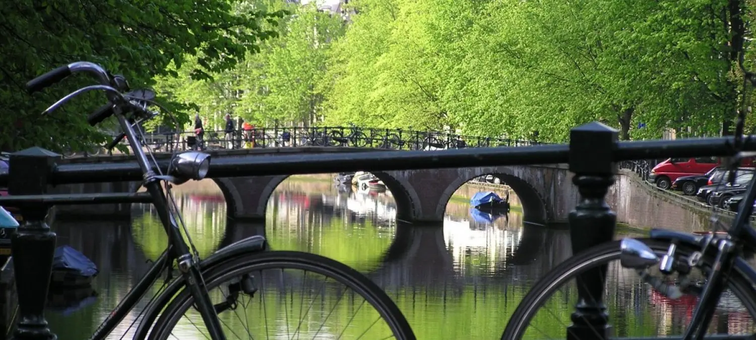 Fietsen aan een Amsterdamse gracht met stenen brug en groene kadebomen