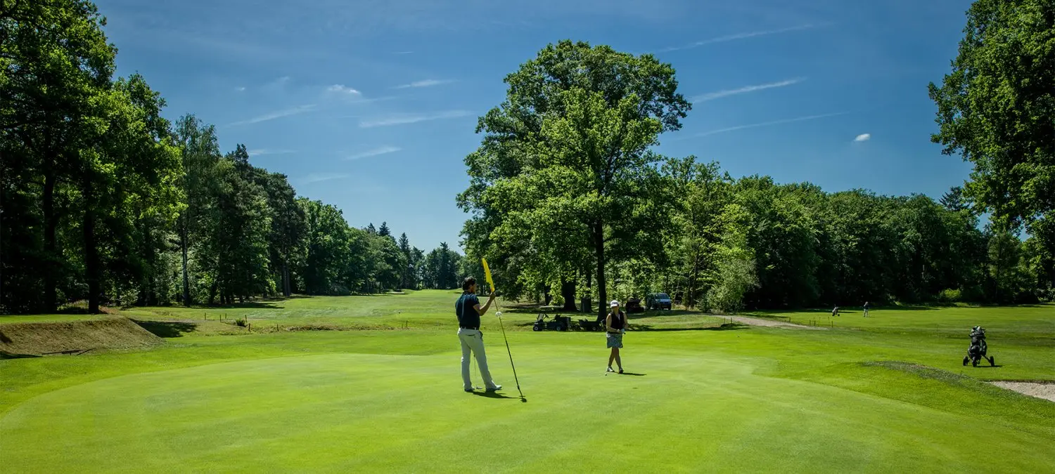 Twee golfers op een green met bomen op de achtergrond