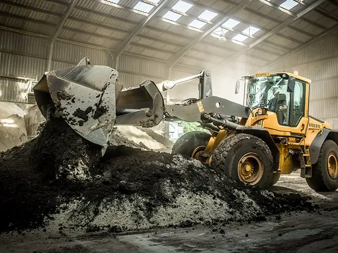 Gele shovel kiept donkere grond uit de bak in een open loods