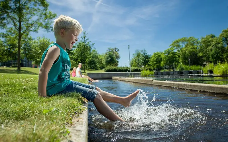Jongen plenst met zijn voeten in een waterloop in het park