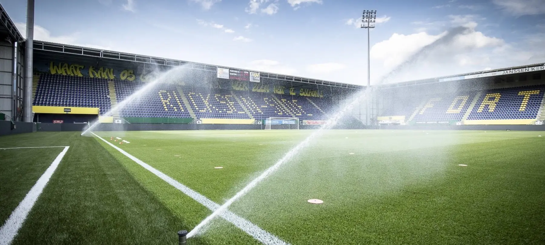 Sproeiers bevochtigen een voetbalveld voor lege tribunes