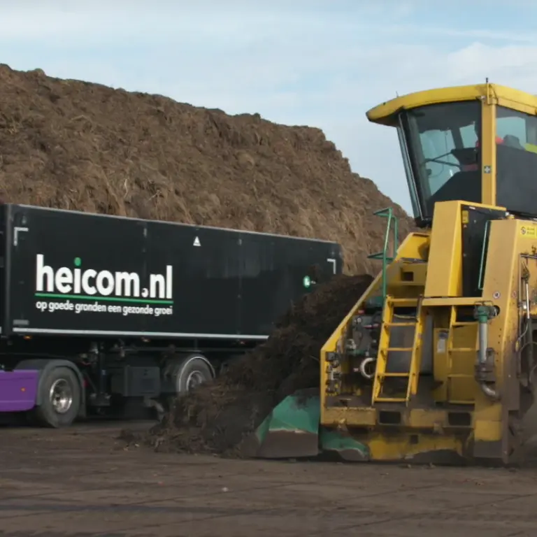 Compostkeerder bewerkt een composthoop naast een paarse Heicom-vrachtwagen