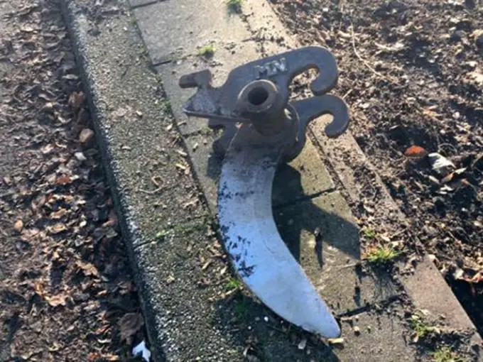 Gebogen metalen mes van een grondbewerkingsmachine op een stoeprand
