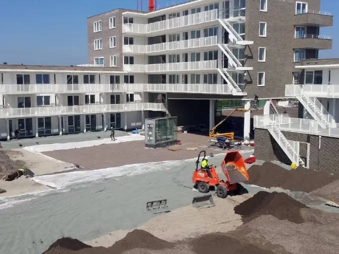 Dumper met oranje kiepbak tussen grondhopen op een binnenterrein in aanbouw