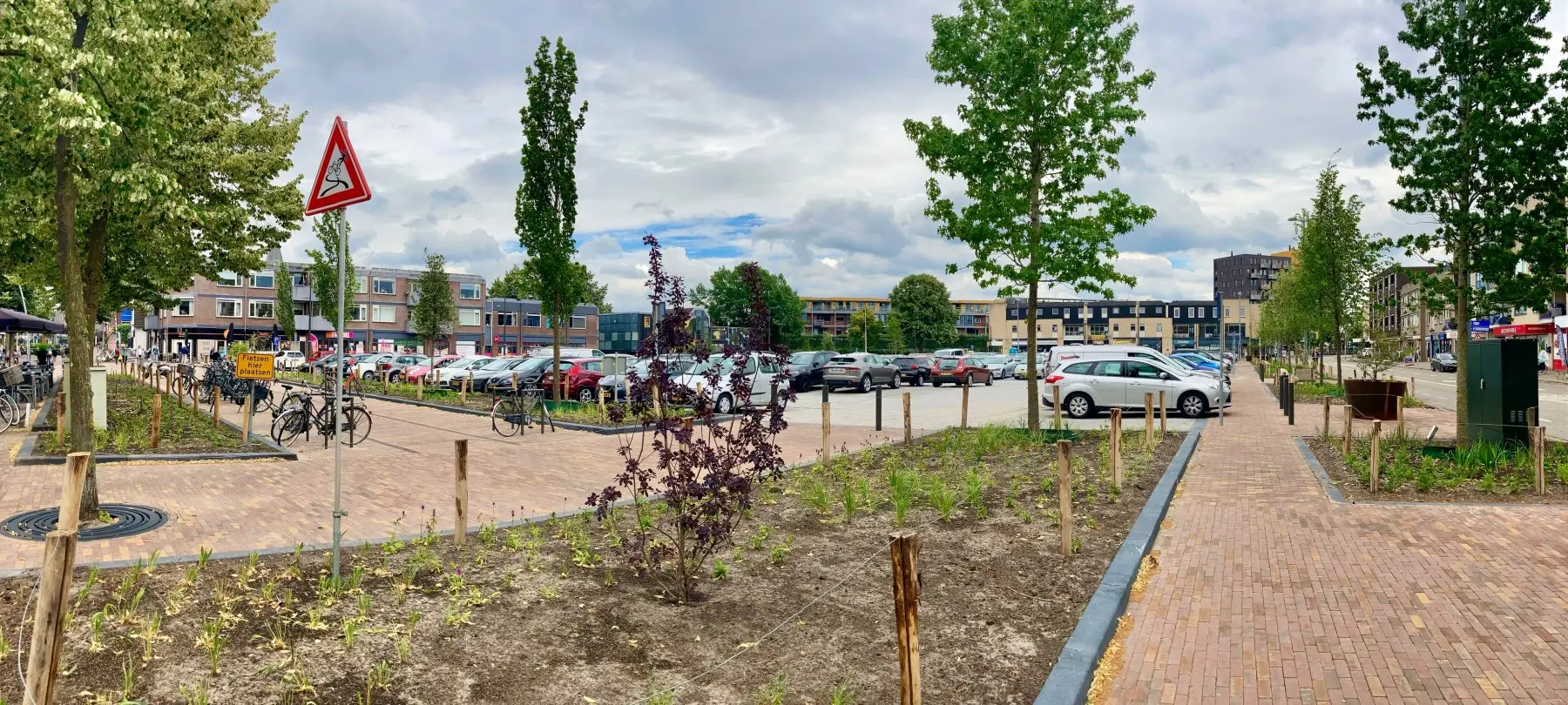 Plein met jonge bomen en pas ingeplante vakken naast een parkeerterrein