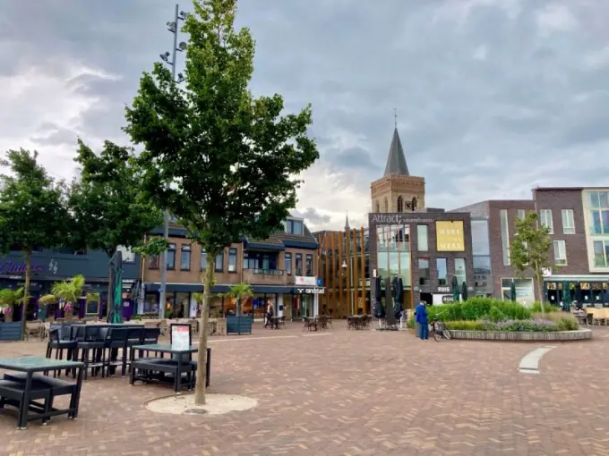 Bestraat marktplein met jonge bomen, terrasmeubels en een kerktoren