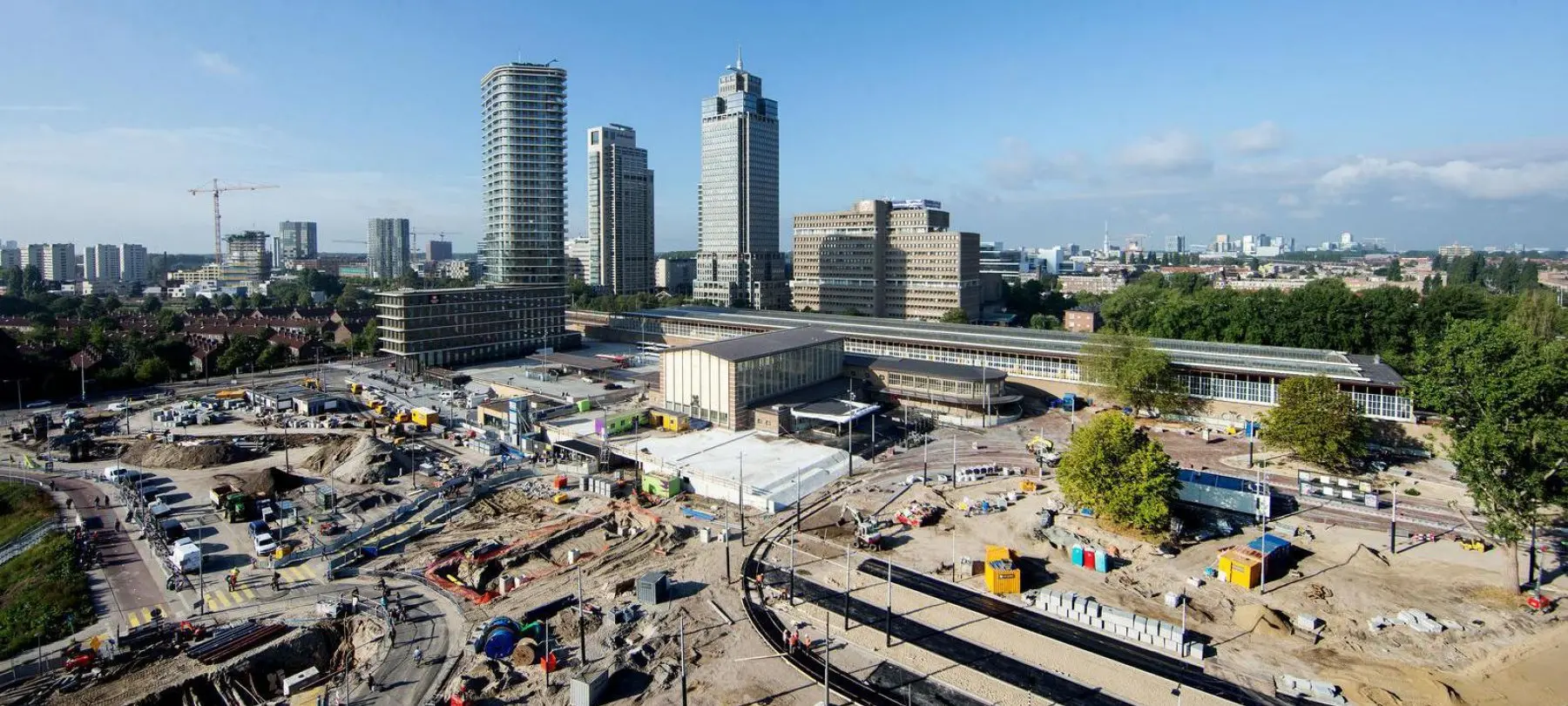 Groot bouwterrein voor een stationsgebouw met hoogbouw op de achtergrond