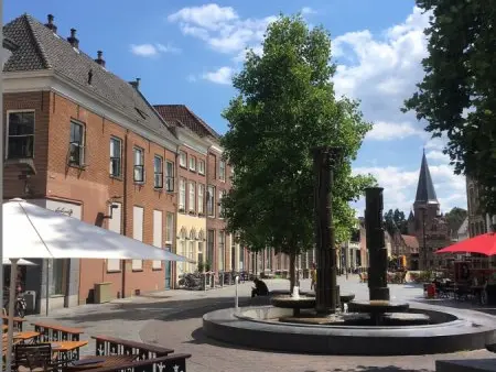 Fontein en boom op een plein met historische panden en kerktoren