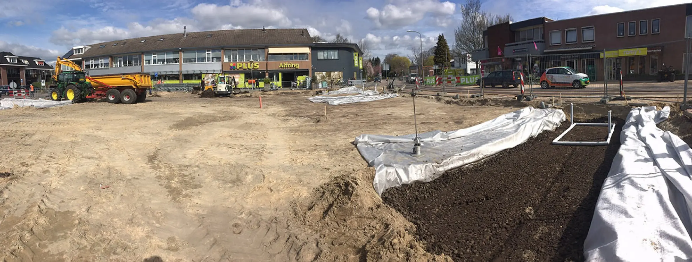 Zandvlakte in aanleg met tractor, kipwagen en rollen doek bij een supermarkt