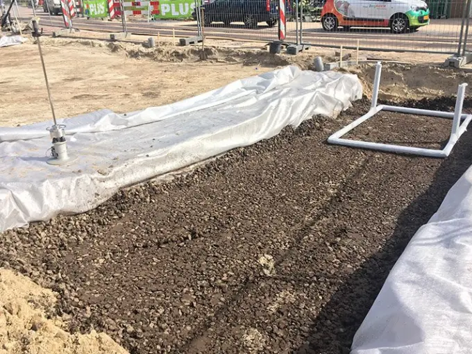 Sleuf gevuld met donkere grond tussen wit worteldoek op een bouwterrein