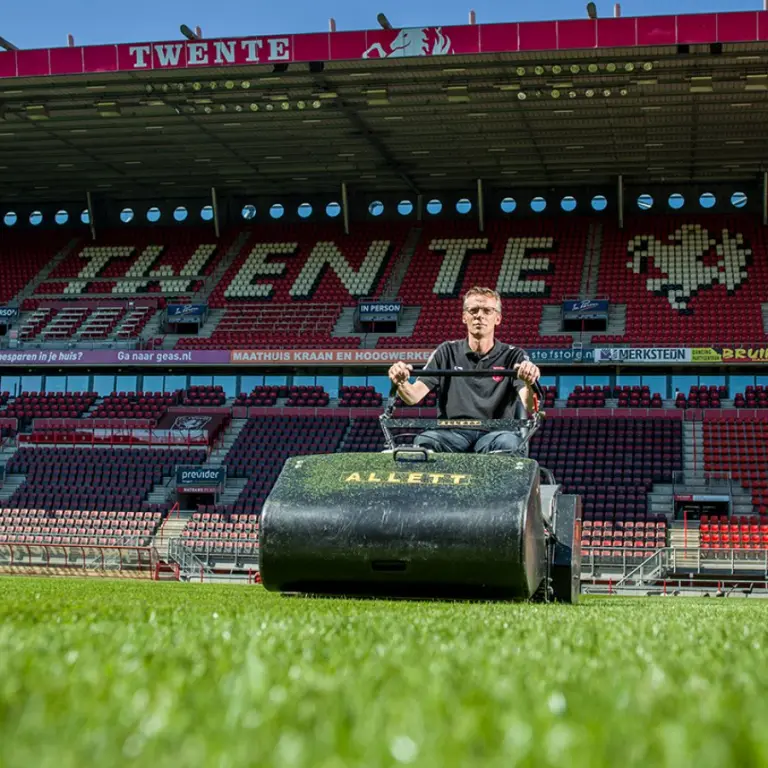 Terreinknecht op een maaimachine op het gras van een leeg voetbalstadion