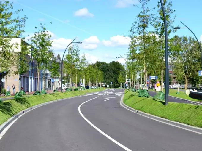 Nieuwe asfaltweg met jonge bomen en groene gietzakken in de bermen