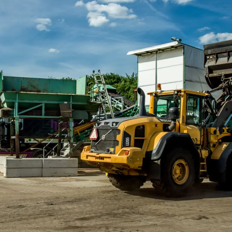 Shovel met geheven bak naast een vrachtwagen en zeefinstallatie op een bedrijfsterrein