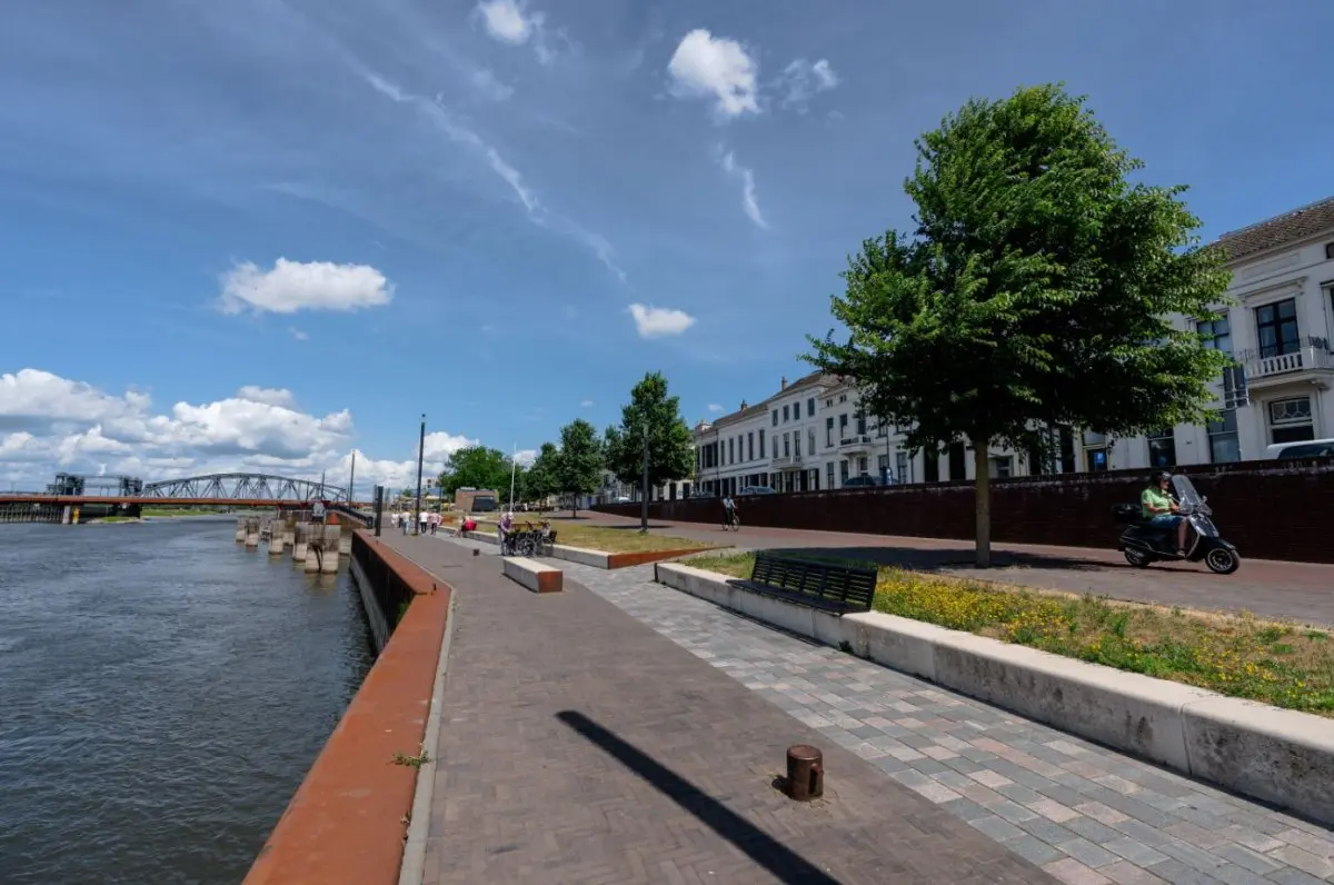 Kade met zitbank en scooter langs de rivier bij een oude spoorbrug