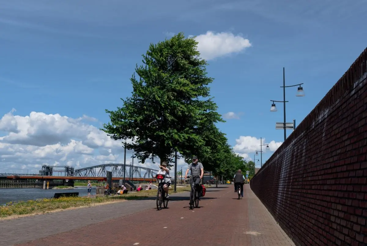 Twee fietsers rijden langs een hoge bakstenen muur met lantaarnpalen