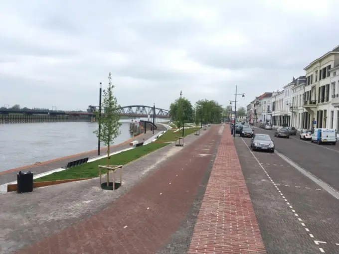 Overzicht van een heringerichte kade met jonge bomen langs de rivier