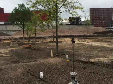 Jonge bomen op een kaal bouwterrein met buizen in de grond