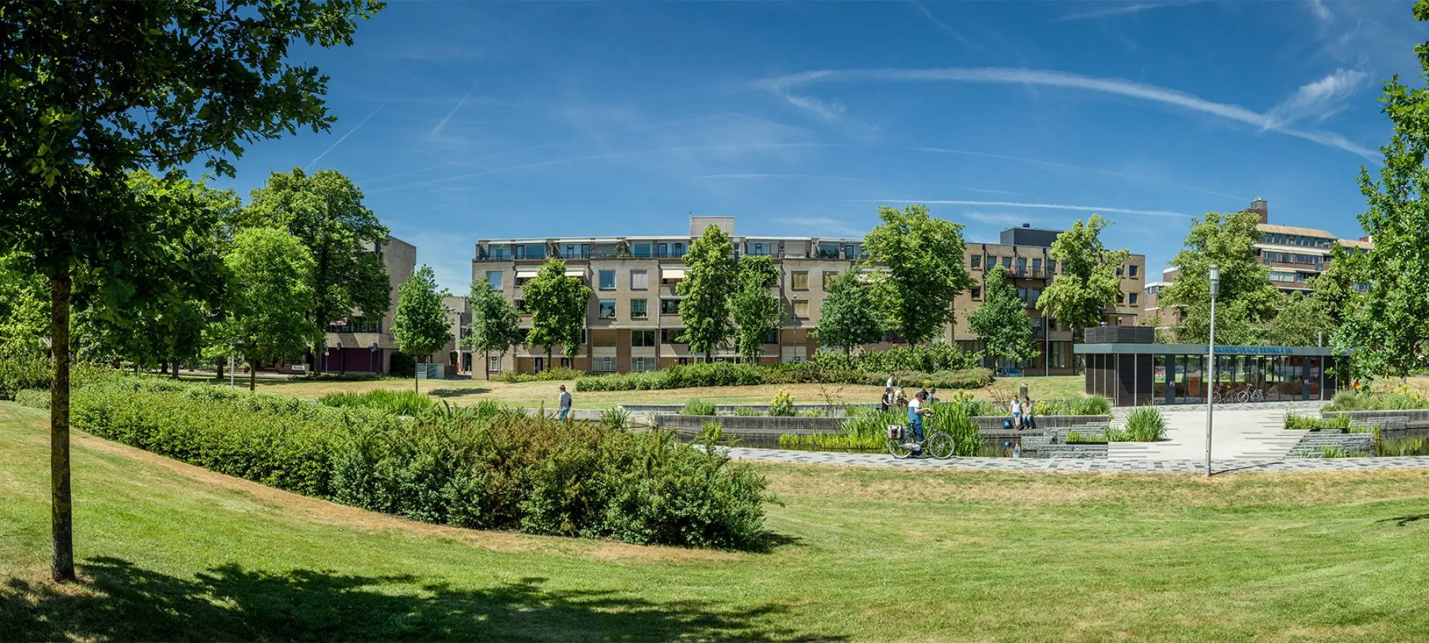Grasveld en beplanting rond een waterpartij voor een woonblok