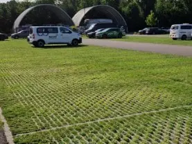 Bestelbus en auto's op een grasparkeerplaats bij twee ronde hallen