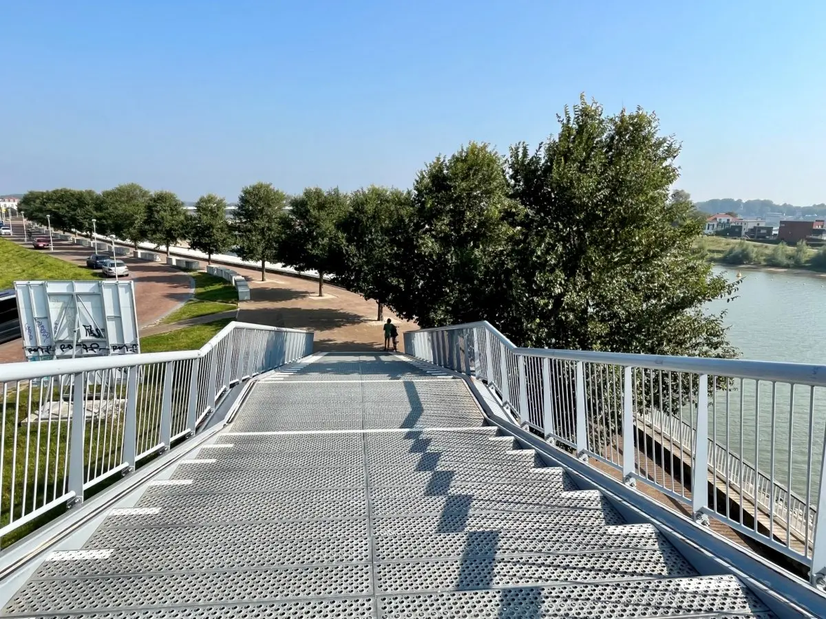 Stalen trap van een brug naar een promenade langs de rivier