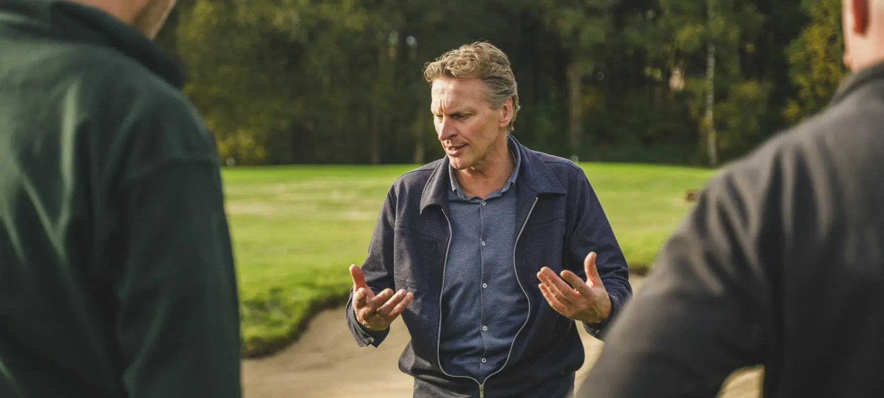 Man praat met twee mannen bij een zandbunker op een golfbaan