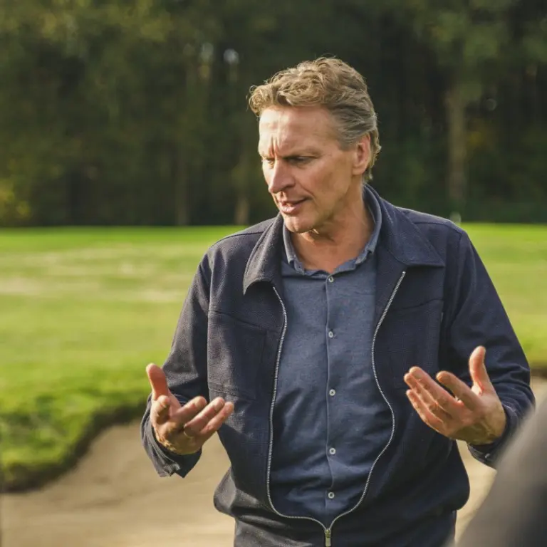 Man praat met twee mannen bij een zandbunker op een golfbaan