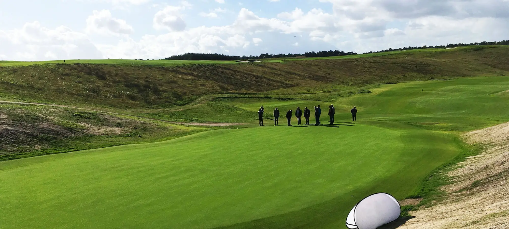 Groepje mensen op een green tussen de duinachtige heuvels van een golfbaan
