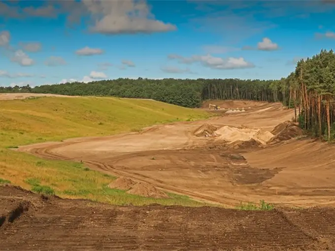 Golfbaan in aanleg met uitgegraven zandvlakken langs een dennenbos