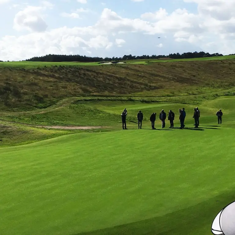 Groepje mensen op een green tussen de duinachtige heuvels van een golfbaan