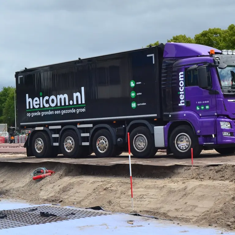 Paarse vrachtwagen met het opschrift heicom.nl op een bouwterrein