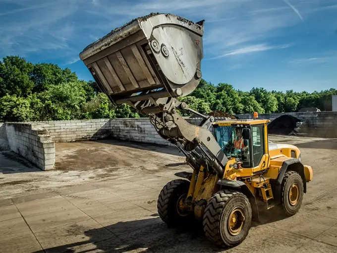 Gele shovel met geheven bak op een terrein met betonnen keerwanden