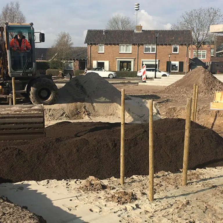 Graafmachine en werkmannen leggen een plantvak met donkere grond aan