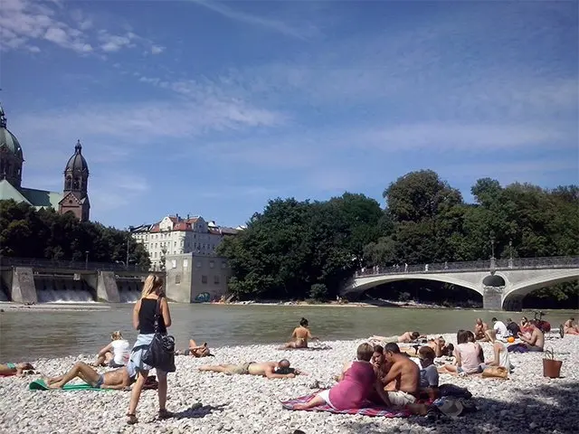 Mensen zonnen op een kiezelstrand langs een rivier in de stad