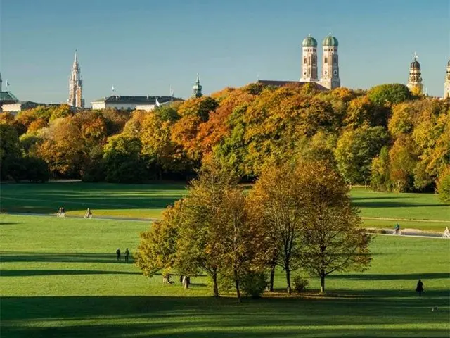 Groot stadspark met herfstkleurige bomen en kerktorens aan de horizon