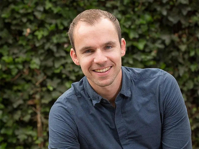 Portret van Hans van der Weerd in donkerblauw overhemd bij klimop